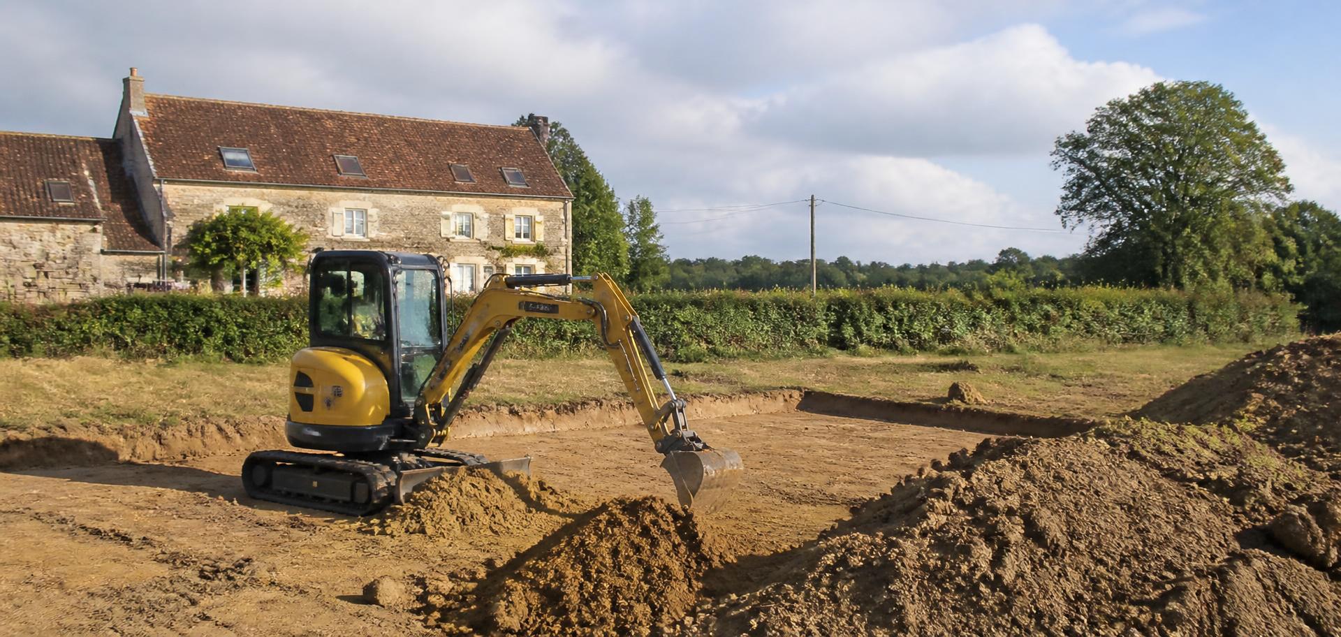 Mini-pelle déplaçant de la terre sur un chantier de terrassement dans la campagne du Gâtinais