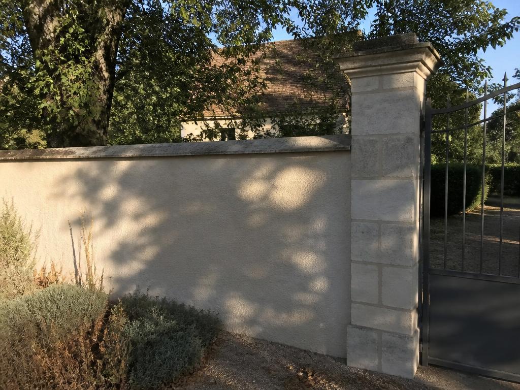 Mur de clôture enduit avec chaperon et pilier de portail en pierre