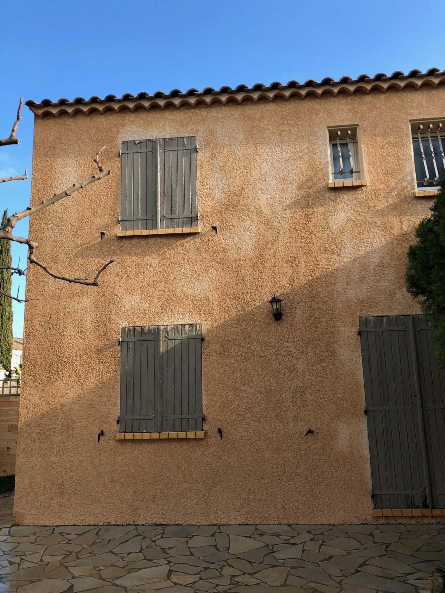 Pignon de maison en enduit ocre nettoyé avec terrasse en dallage