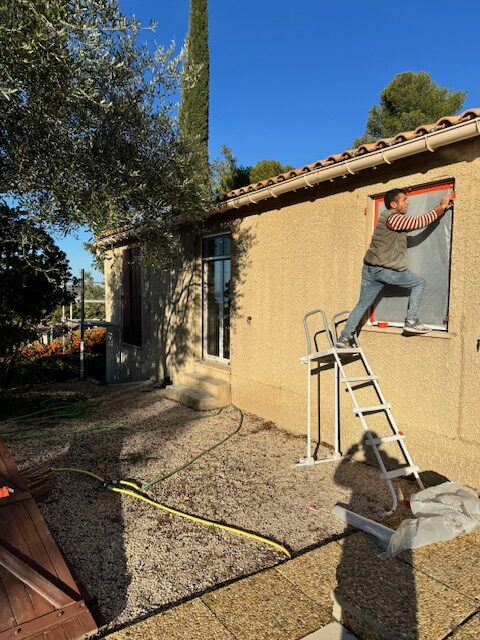 Artisan traitant une façade en enduit gratté autour d'une ouverture